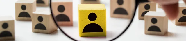 Lupe vor einigen Holzklötzen mit Personen-Icons